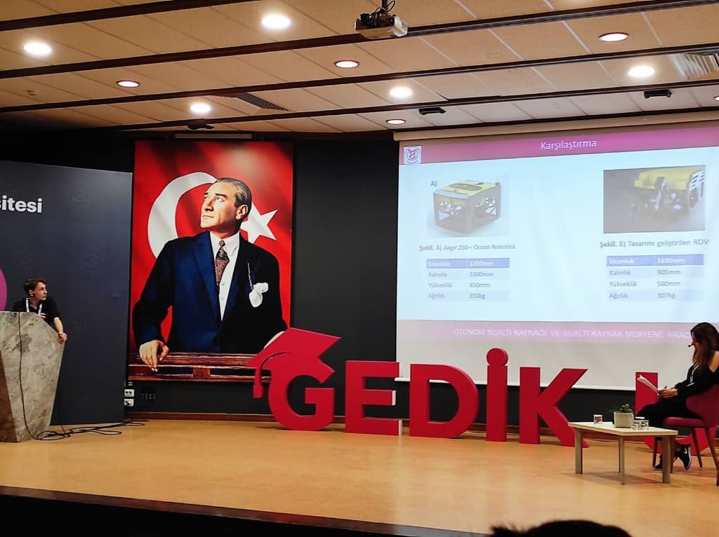 DYUK’22 kongre sahnesinde sunulan karşılaştırma slaytı: ticari Aegir 250 ROV ile tasarımı geliştirilen ROV’un uzunluk, kalınlık, yükseklik ve ağırlık değerleri yan yana